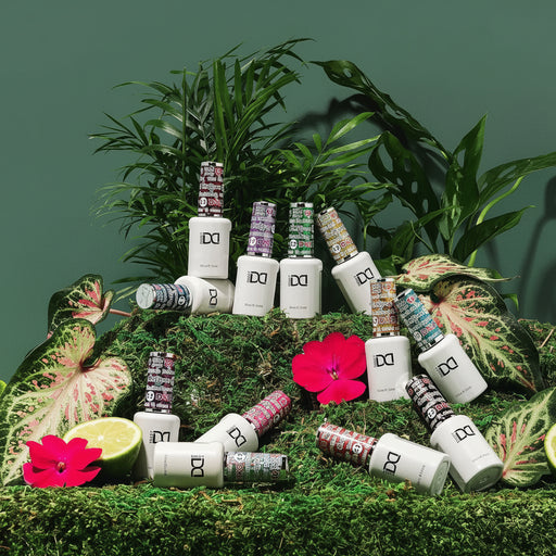 Collection of nail polish bottles arranged on a green surface with plants and flowers.